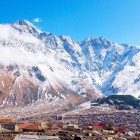 Stepantsminda stretches at the foot of the snow-covered Caucasus Mountains, with houses gathered in the valley and towering peaks surrounding the landscape.