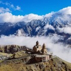 Spectacular view of the Gergeti Trinity Church, perched among the Caucasus Mountains with the imposing Mount Kazbek in the background and clouds drifting through the valley.