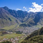 View of Stepantsminda resting in the valley at the foot of the Caucasus Mountains, surrounded by the towering peaks that shape the Kazbegi landscape.