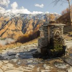 Ancient stone fountain near Gergeti Church, with spring water flowing among the Caucasus mountains and wide-open views over the Kazbegi valley.