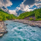 The blue waters of the Adishchala River flow gently below Mount Shkhara, as morning light reveals Upper Svaneti and the quiet village of Adishi.