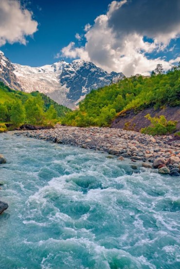 The blue waters of the Adishchala River flow gently below Mount Shkhara, as morning light reveals Upper Svaneti and the quiet village of Adishi.