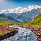 A mountain river flows at the foot of the Tetnuldi glacier, under the clear light of summer. From Chkhunderi Pass, wide views open over Upper Svaneti and the peaks of the Caucasus.