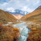 The Enguri River, with its milky waters, flows through a golden valley in Svaneti. It runs through silence and gentle slopes, with the Caucasus peaks as a backdrop.