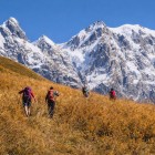 Trekking through golden grasses at the foot of the Shkhara glacier in Svaneti. The trail climbs through silence and open views, while snow-capped peaks accompany every step.