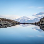 Lake Udziro, among high-altitude rocks, reflects the snow-capped peaks of the Caucasus. Calm waters and clear skies shape a quiet, essential landscape.
