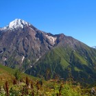 Trail through high-altitude meadows in Lentekhi, with views over the Caucasus mountains. Green slopes and rocky ridges follow the path in a wide, open landscape.
