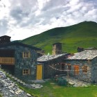 Traditional stone guesthouse in Svaneti, set among green meadows and the Caucasus mountains. Authentic atmosphere, warm lights at sunset and quiet mountain life.