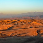 Golden hills of the Agafay Desert lit by the sunset, with the Atlas Mountains rising in the background of Morocco.
