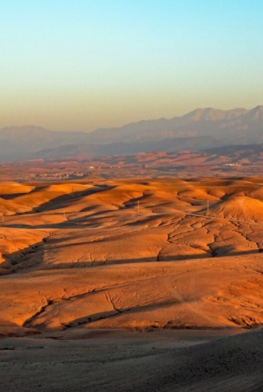 Golden hills of the Agafay Desert lit by the sunset, with the Atlas Mountains rising in the background of Morocco.