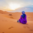 Traveller sitting on the dunes of Merzouga while watching the sun rise over the Sahara, surrounded by silence, golden sand and endless desert views.