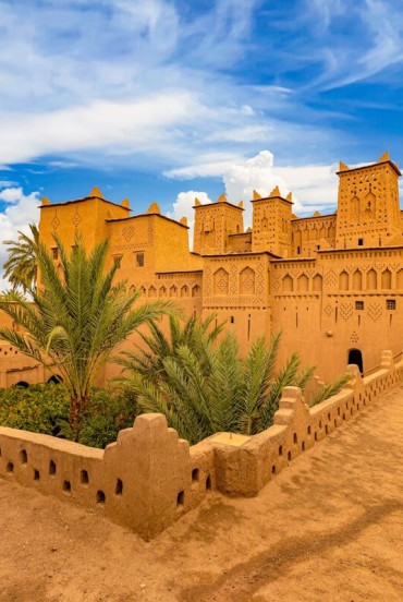 View of a traditional kasbah in Ouarzazate, among ochre-coloured walls, inner courtyards, palm trees and details of Moroccan Berber architecture.