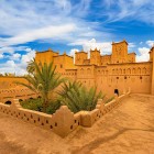 View of a traditional kasbah in Ouarzazate, among ochre-coloured walls, inner courtyards, palm trees and details of Moroccan Berber architecture.