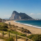 Golden sands stretch along Gibraltar's coastline toward the iconic Rock, where the Mediterranean meets the Atlantic, creating a breathtaking and unforgettable seascape.