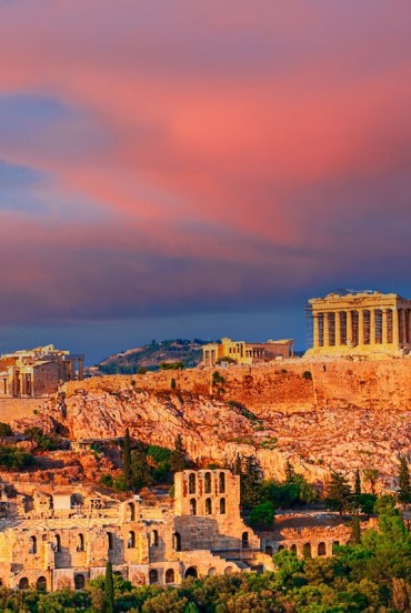 At sunset, the Acropolis rises above Athens with the Parthenon glowing in warm pink hues. A breathtaking panorama celebrating over two thousand years of Greek history.
