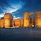 Ávila's imposing medieval walls, a UNESCO World Heritage Site, glow at dusk, framing the historic Puerta del Alcázar, the iconic gateway to Spain's best-preserved fortified city.