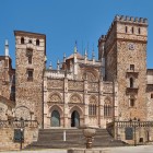 The Gothic-Mudéjar façade of the Royal Monastery of Santa María de Guadalupe overlooks the village square, with crenellated towers and refined carvings in Extremadura.