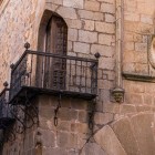 A wrought-iron balcony projects from a stone façade in Cáceres’ historic centre, beside a noble coat of arms that recalls the aristocratic past of the medieval city.