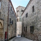A narrow paved street in Trujillo’s historic centre runs beside stone noble palaces and carved portals, leading the eye towards the Romanesque tower of Santa María la Mayor.