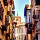 Calle de San Bartolomé reveals authentic Toledo through iron balconies, historic houses and the church’s Mudéjar apse, beside Pantoja y Angulo Palace.