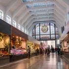 Inside Mercado de la Ribera, fresh produce stalls enliven the vast Art Deco hall, illuminated by stained-glass windows and bright white structural ribs.