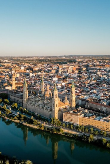 Aerial view of Zaragoza along the Ebro: the Basilica del Pilar dominates the historic centre with its towers and domes, a monumental and spiritual symbol of the Aragonese city.