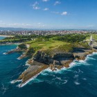 Aerial view of Cabo Mayor, where the lighthouse overlooks cliffs sculpted by the Cantabrian Sea, amid green meadows and coves, with Santander in the background.