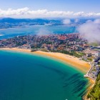 Aerial view of Santander and El Sardinero Beach, a long golden shoreline washed by the Cantabrian Sea, amid coastal districts, green peninsulas and hills.
