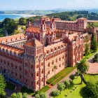 The Pontifical University overlooks Comillas with brick towers, Neo-Gothic and Modernist details, surrounded by gardens and the green landscape of the Cantabrian coast.