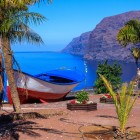 A traditional boat framed by palm trees draws the eye toward Los Gigantes Bay, where the blue Atlantic meets spectacular volcanic cliffs.