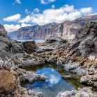 Among volcanic rocks sculpted by the ocean, a natural pool reflects Tenerife’s sky, while the imposing Los Gigantes cliffs dominate the horizon.