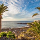 Playa de La Arena, in Puerto de Santiago, unfolds amid palm trees and volcanic rocks, with its black sand washed by the Atlantic and illuminated by warm sunlight.