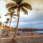 At Playa de La Arena, in Puerto de Santiago, palm trees and parasols line the black volcanic-sand beach overlooking the Atlantic beneath an evocative sunset sky.