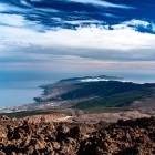 From the heights of Mount Teide, the view descends from dark lava flows to the green Corona Forestal, reaching the towns along Tenerife’s southern coast and the vast Atlantic Ocean.