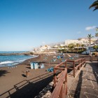 The promenade of Playa de La Arena, in Puerto de Santiago, runs alongside its distinctive black-sand beach, amid palm trees, panoramic terraces and the blue Atlantic.
