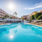 The spacious pool at the 4-star Servatur Isora Suites in Puerto de Santiago invites guests to relax amid sun loungers, palm trees and gardens beneath Tenerife’s bright sky.