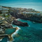 Seen from above, the Isla Cangrejo Natural Pool lies among the volcanic rocks of Puerto de Santiago, surrounded by the turquoise waters of the Atlantic and houses overlooking the coast.
