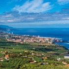 Across the plantations of the fertile Orotava Valley, the view reaches Puerto de la Cruz, a lively resort on Tenerife’s northern coast, framed by the deep blue Atlantic Ocean.