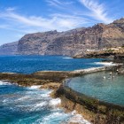 In Puerto de Santiago, a natural pool nestled into the volcanic coastline offers crystal-clear waters, while the Los Gigantes cliffs rise in the background.
