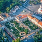 Seen from above, the National Palace of Queluz appears as an elegant royal residence framed by Baroque gardens, ornamental parterres, fountains and long wings with distinctive red roofs.