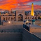 At sunset, the Muhammad Rahim Khan II Madrasa dominates Itchan Kala, while the illuminated Islam Khoja Minaret rises above ancient Khiva.