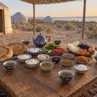 At the yurt camp, an Uzbek breakfast welcomes travelers with non bread, tea, fruit and wholesome dishes, served outdoors in the peaceful morning light of the desert.