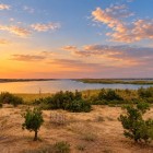 At sunset, Lake Aydarkul reflects the sky’s golden shades, while desert vegetation frames a peaceful and surprising landscape of Uzbekistan.