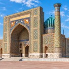 Opposite the Ulugbek Madrasa stands the 17th-century Sher-Dor Madrasa, distinguished by its monumental portal decorated with the famous feline figures and human-faced suns.
