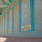 The journey continues beneath the veranda, where turquoise panels and golden geometric motifs decorate the walls and ceiling, leading towards the palace’s historic interiors.