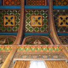The gaze rises towards an ornate wooden ceiling composed of stained-glass panels, carvings and polychrome geometric motifs, revealing the attention devoted to every detail.